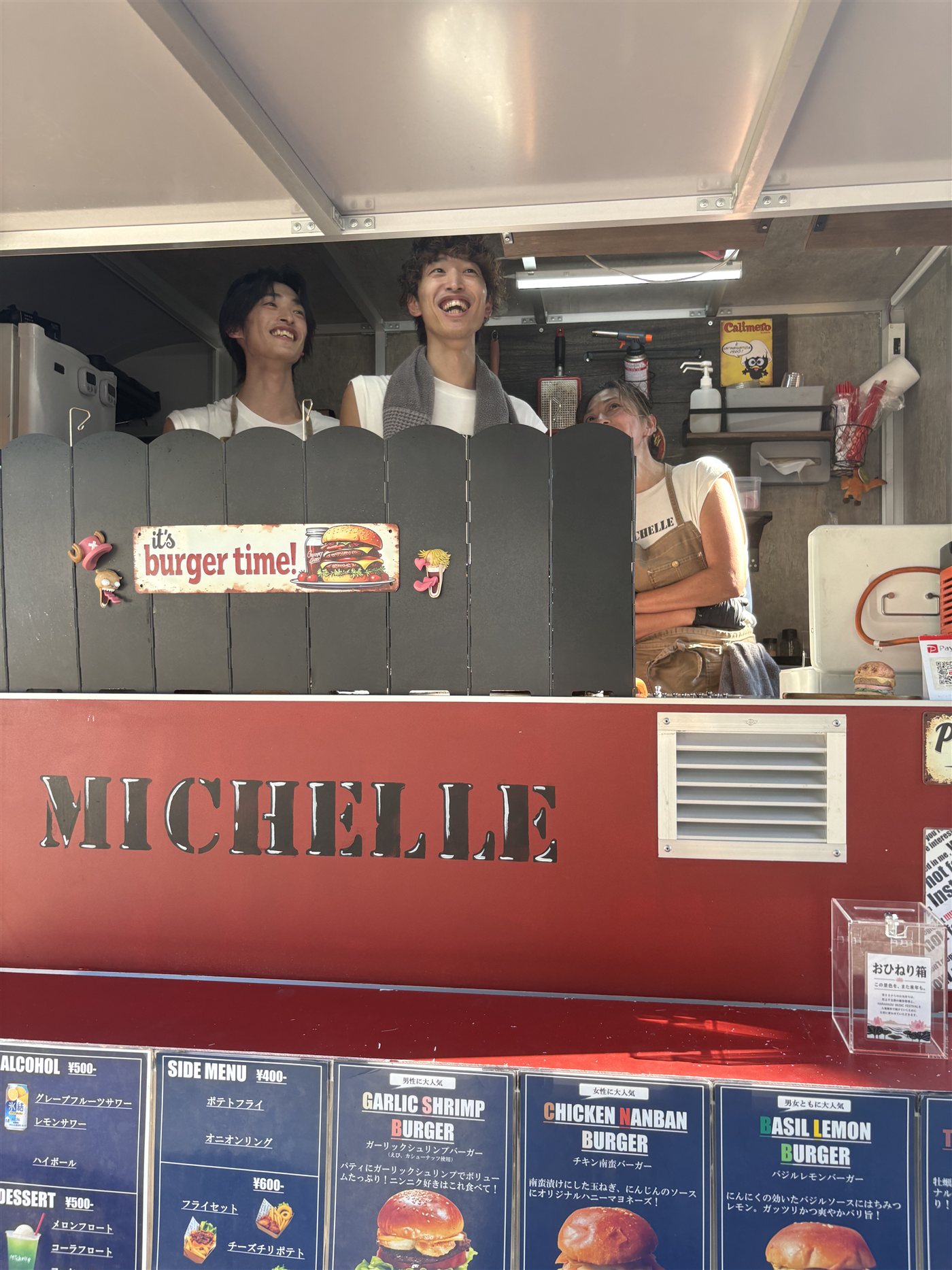 キッチンカーのカウンターで笑う兄弟と、その後ろで働く母